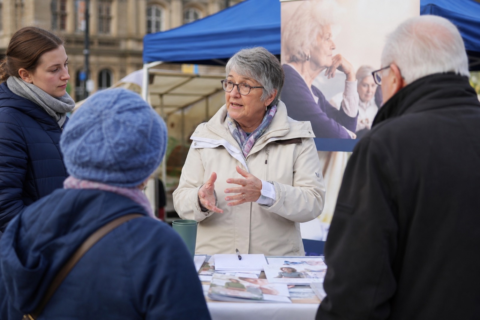 An older spokesperson speaking with the public at an awareness stand about elderly isolation