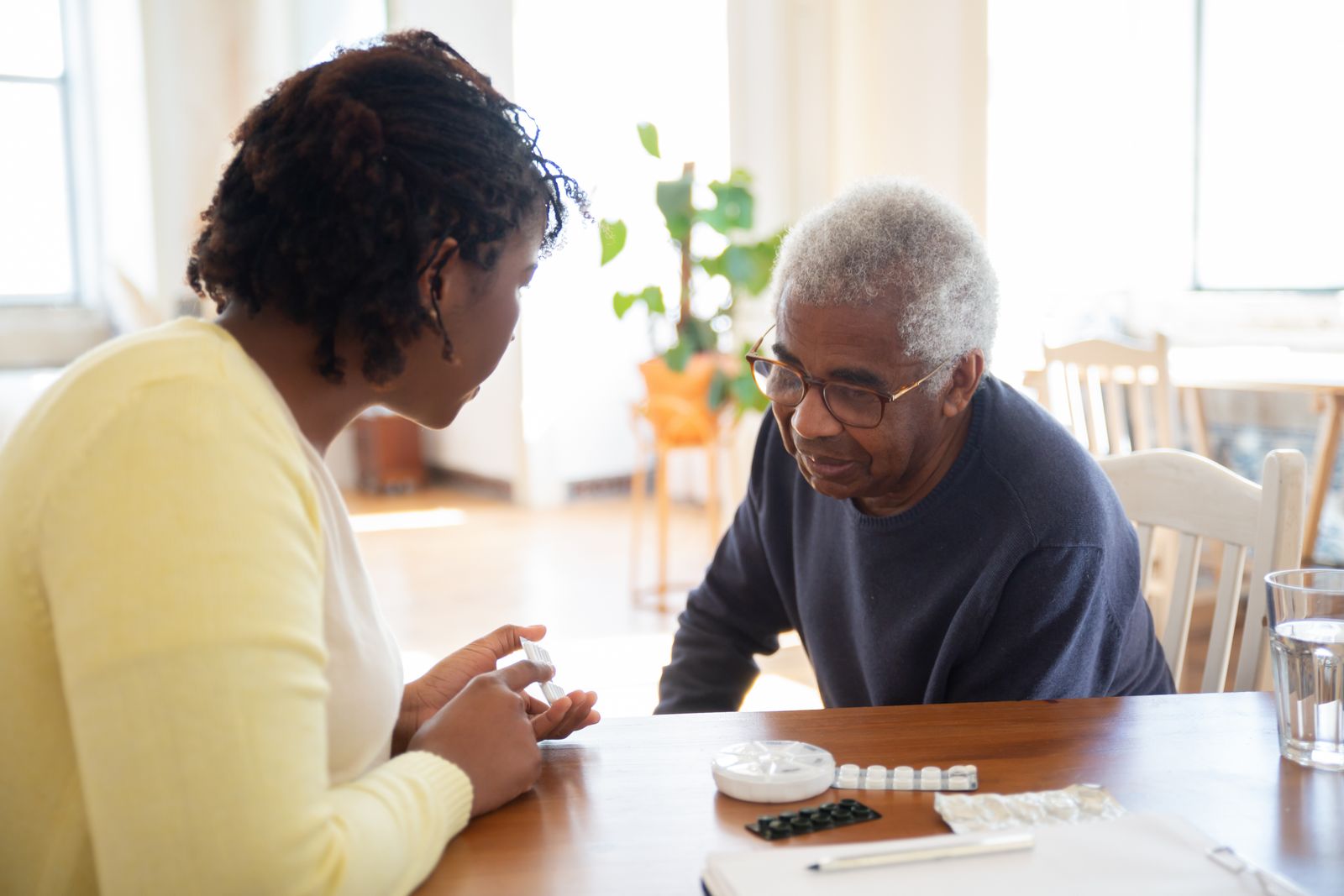 A volunteer helping an older man sort his weekly medication at a table
