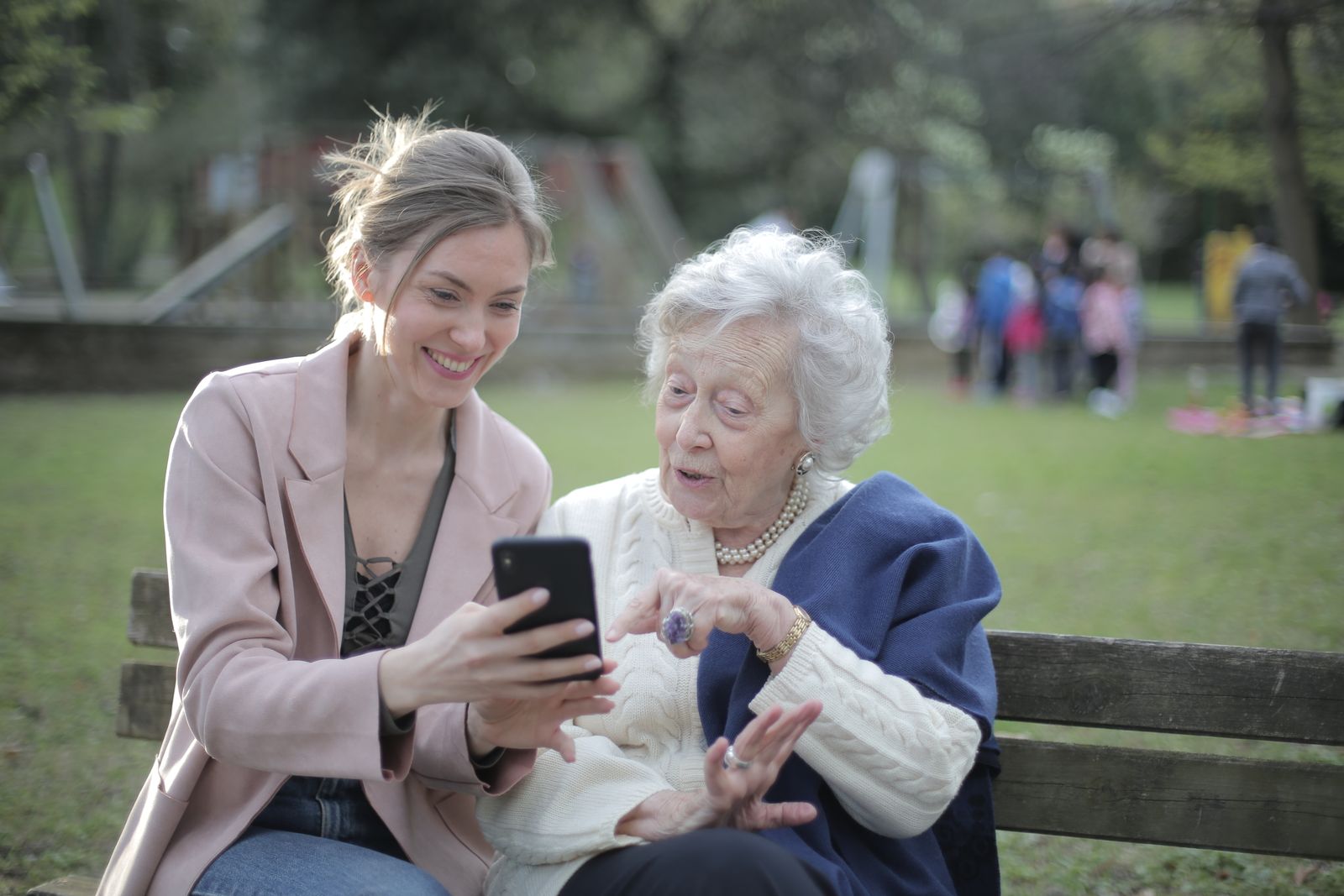 A volunteer and an older woman sitting on a park bench, smiling at a phone together