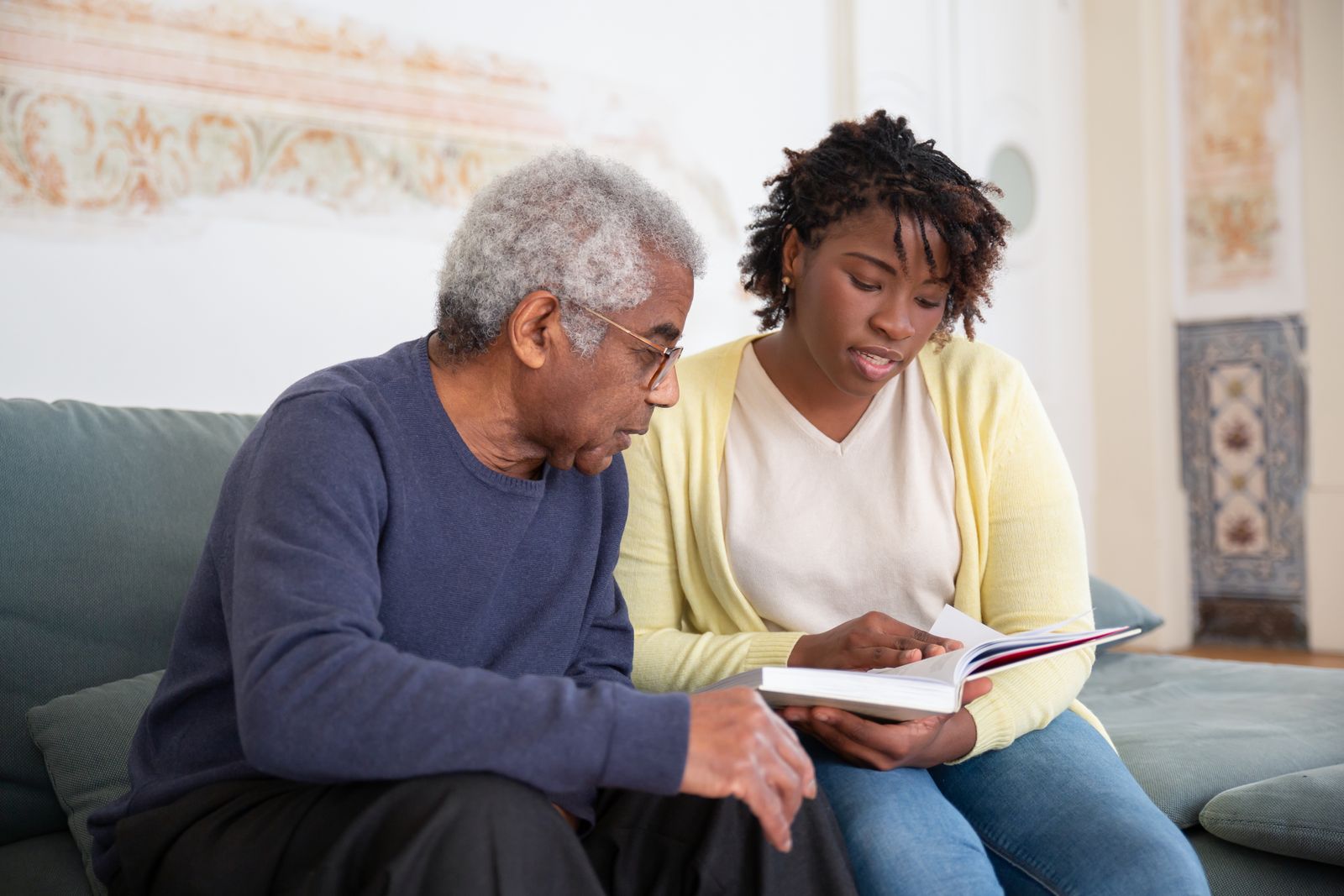 A volunteer reading a book alongside an older man on a sofa